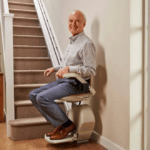 Homme âgé installé dans le fauteuil d'un monte escalier en bas d'un escalier droit étroit